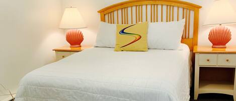 A neatly made bed with a white duvet and a skirted bottom, flanked by two nightstands with lamps and shell-shaped lampshades.