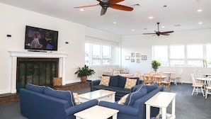 A spacious living room with a fireplace, blue sofas, white tables, and ceiling fans. - Sandcastle Resort and Club (Provincetown)