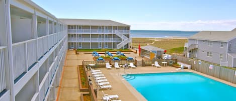 A hotel with a pool, lounge chairs, and a view of the beach.
