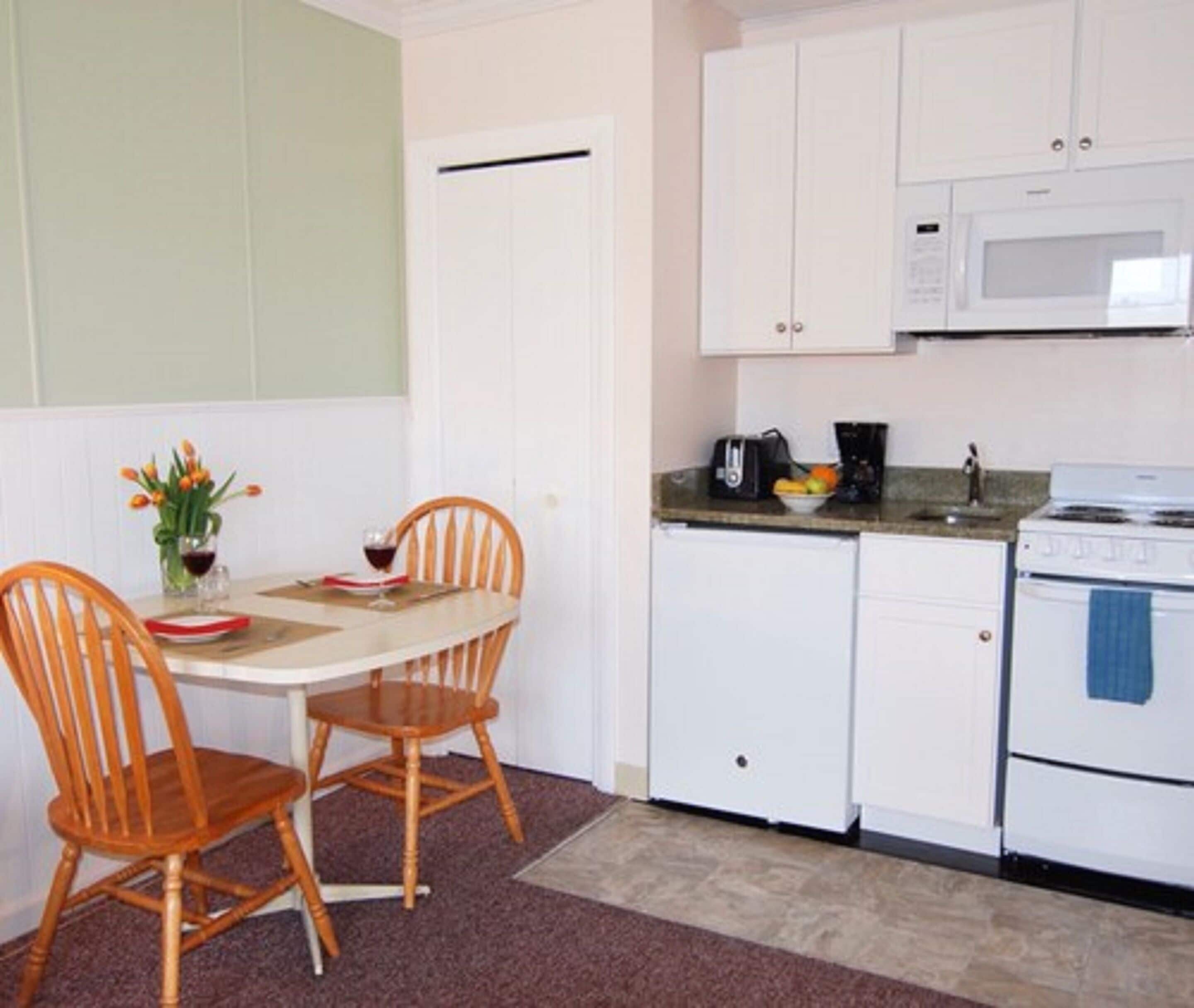 A compact kitchen with white cabinets, a microwave, a stove, and a dining table with two chairs.
