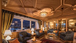 Une pièce chaleureuse avec des canapés à motifs, un plafond en bois et une grande fenêtre agrémentée de rideaux.