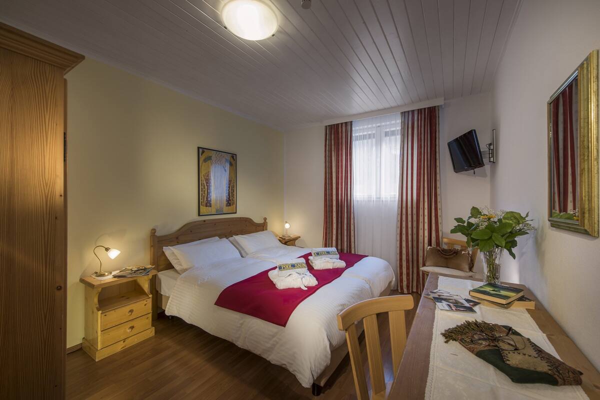 Un dormitorio ordenado con cama de madera, mesitas de noche, un escritorio pequeño y una silla.