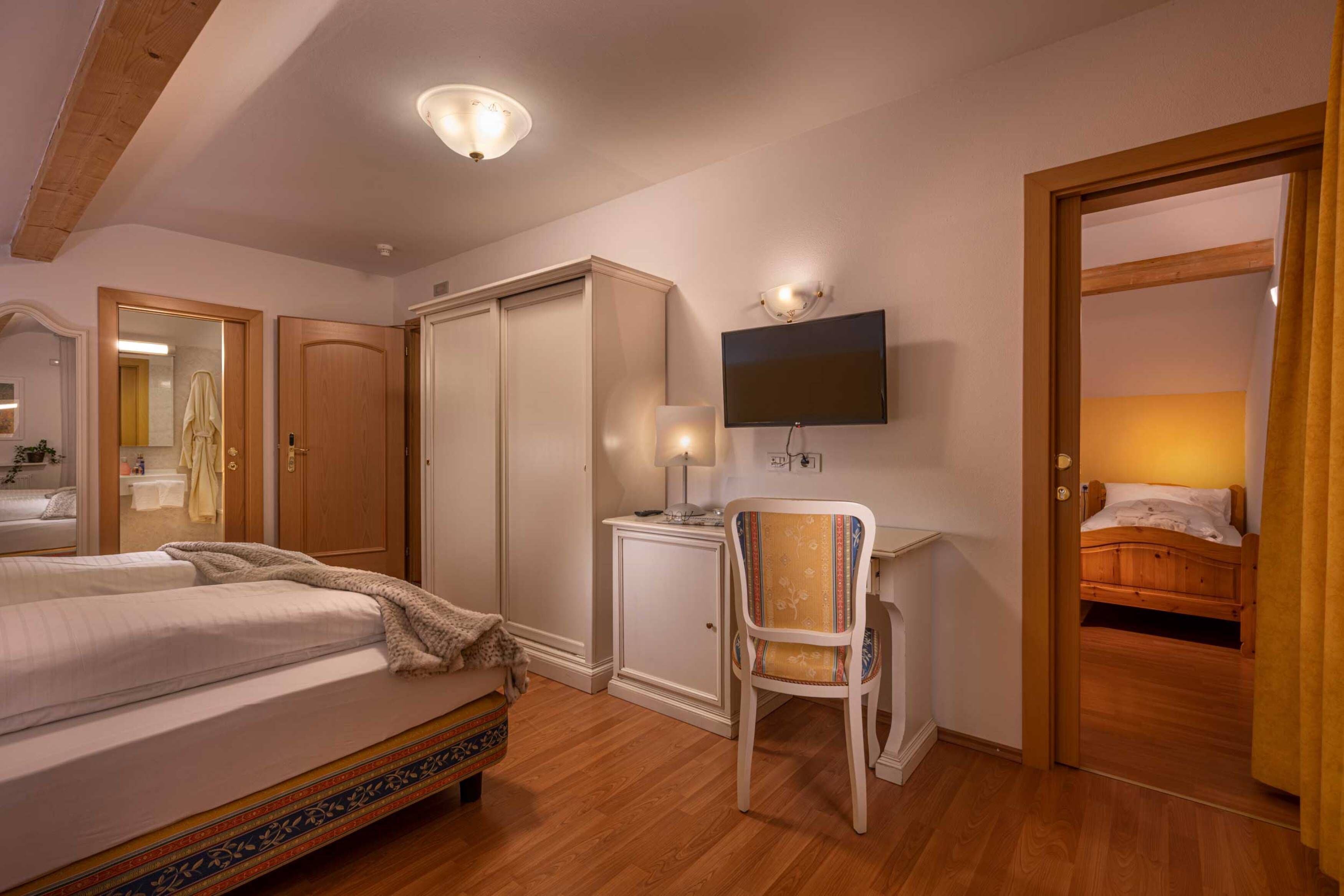 A hotel room with a bed, a desk with a computer, a chair, a television, and a wardrobe.