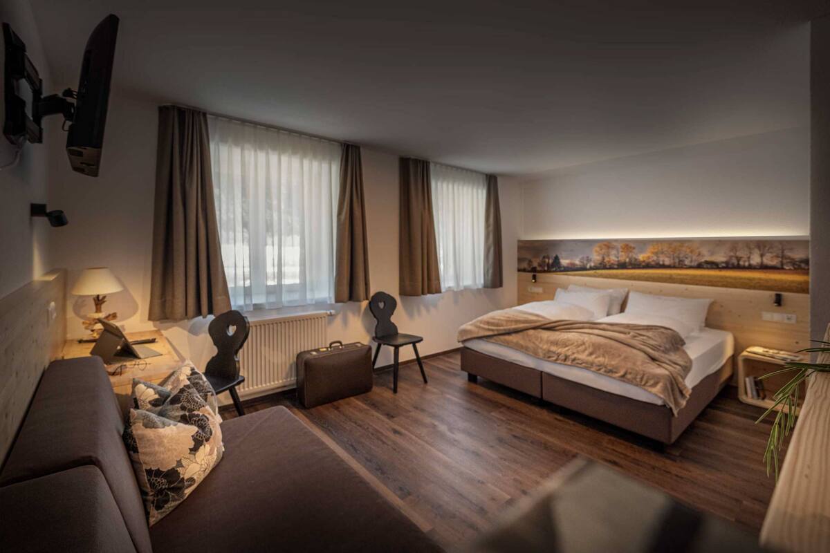 Una habitación de hotel con cama, escritorio, silla, radiador y ventana con cortinas.