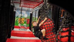 A child climbing a rope net structure in an indoor play area with red steps and a green wall with cartoon characters. - Thermenhotel Kurz (Lutzmannsburg)