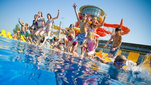 Une piscine où des gens sautent dans l’eau, un toboggan aquatique et une tour de surveillance pour les sauveteurs.