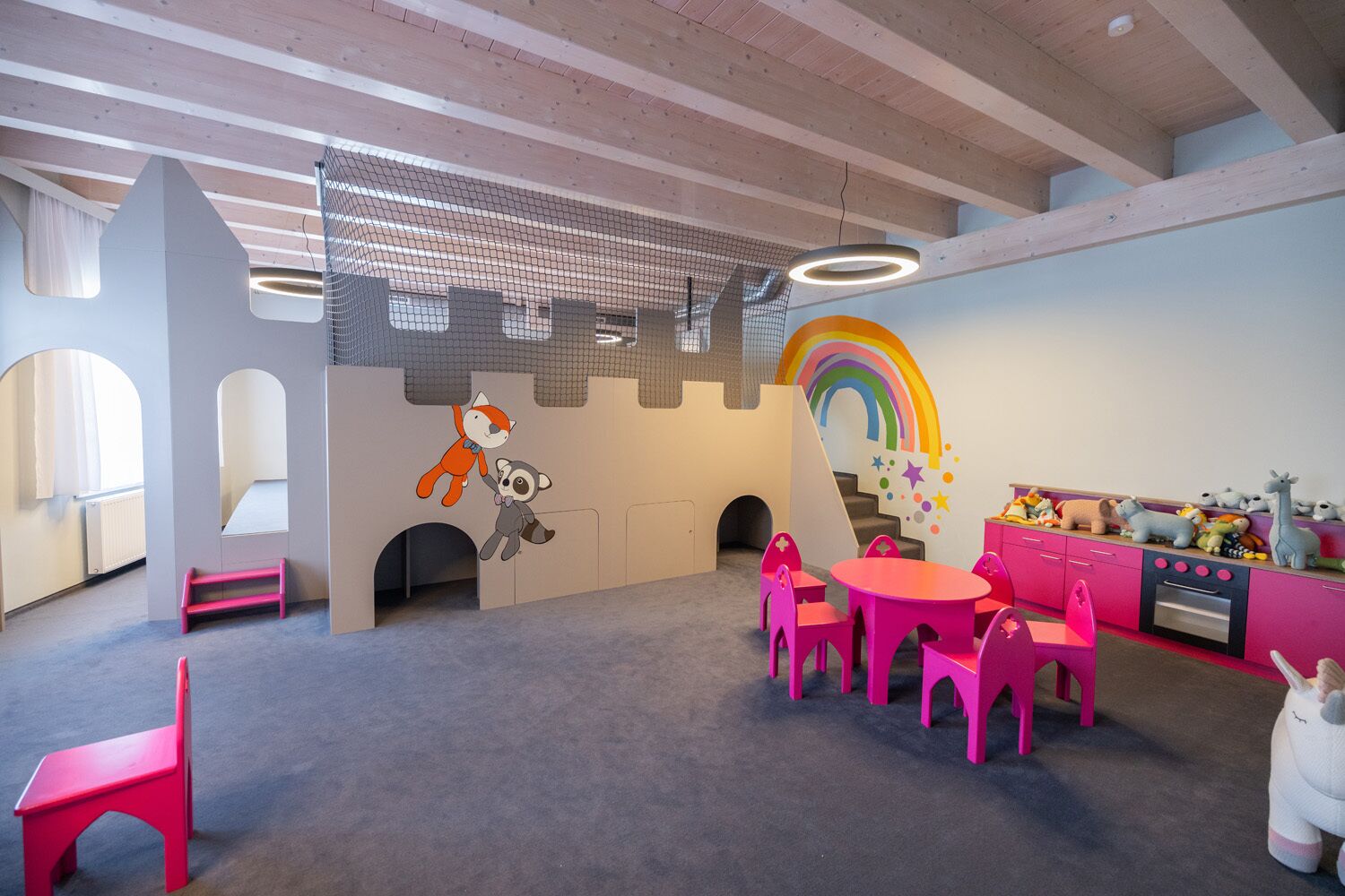 Uma sala de brinquedos infantil com área de recreação temática de castelo, mural de arco-íris e exposição de brinquedos.