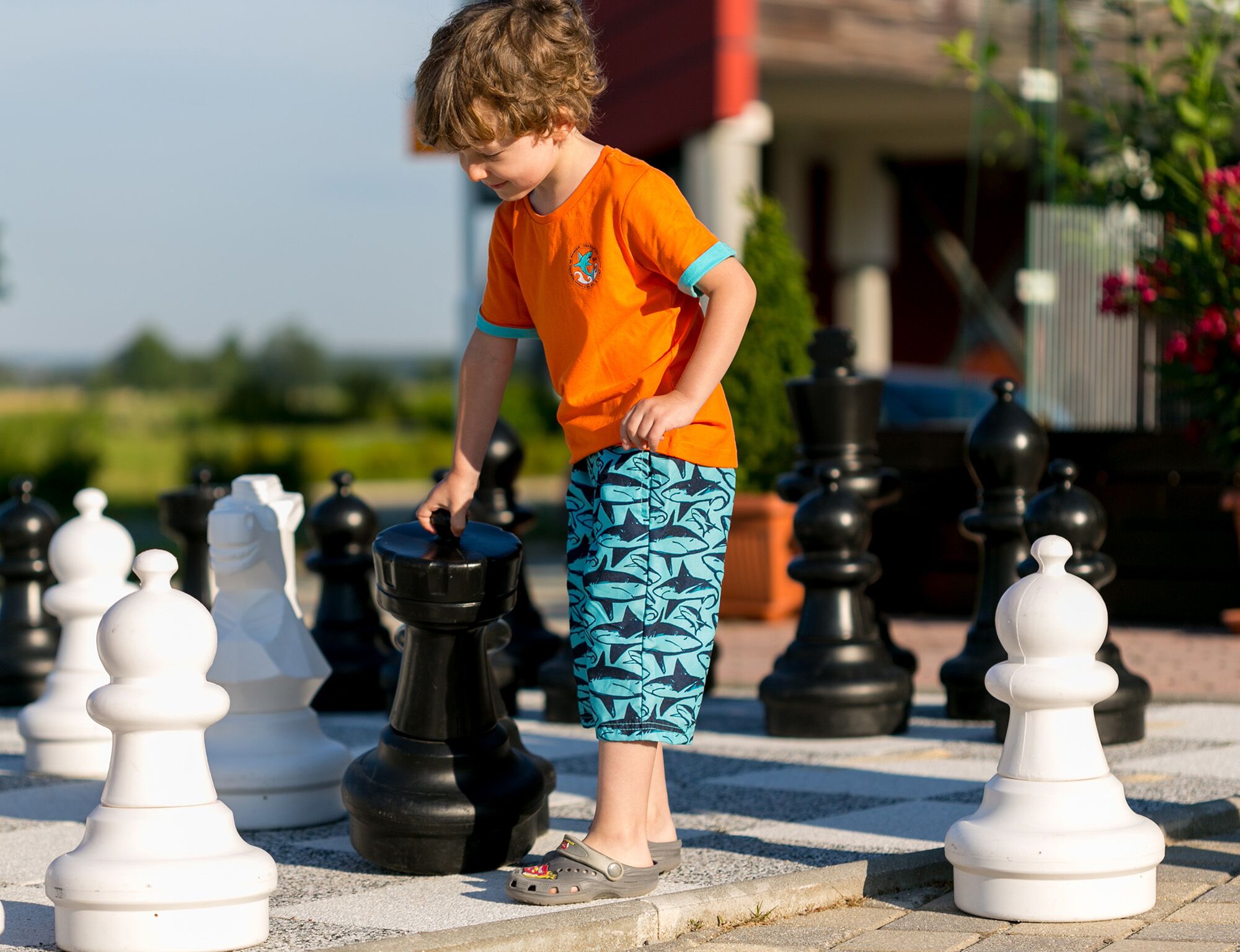 A child playing chess on a paved outdoor area with chess pieces arranged in rows.