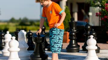 A child playing chess on a paved outdoor area with chess pieces arranged in rows.