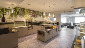 A modern kitchen with a central island, a buffet area with food containers, and a seating area with a sofa and table. - Thermenhotel Kurz (Lutzmannsburg)