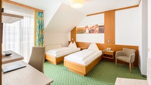 Une chambre d’hôtel avec deux lits simples, un bureau avec une chaise, une petite table et une chaise.