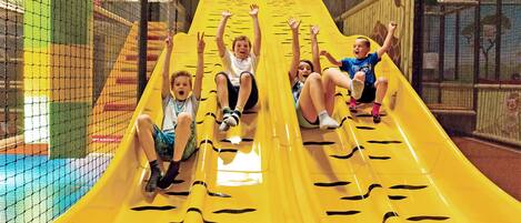 A group of children sliding down a yellow indoor slide with black tiger stripes.