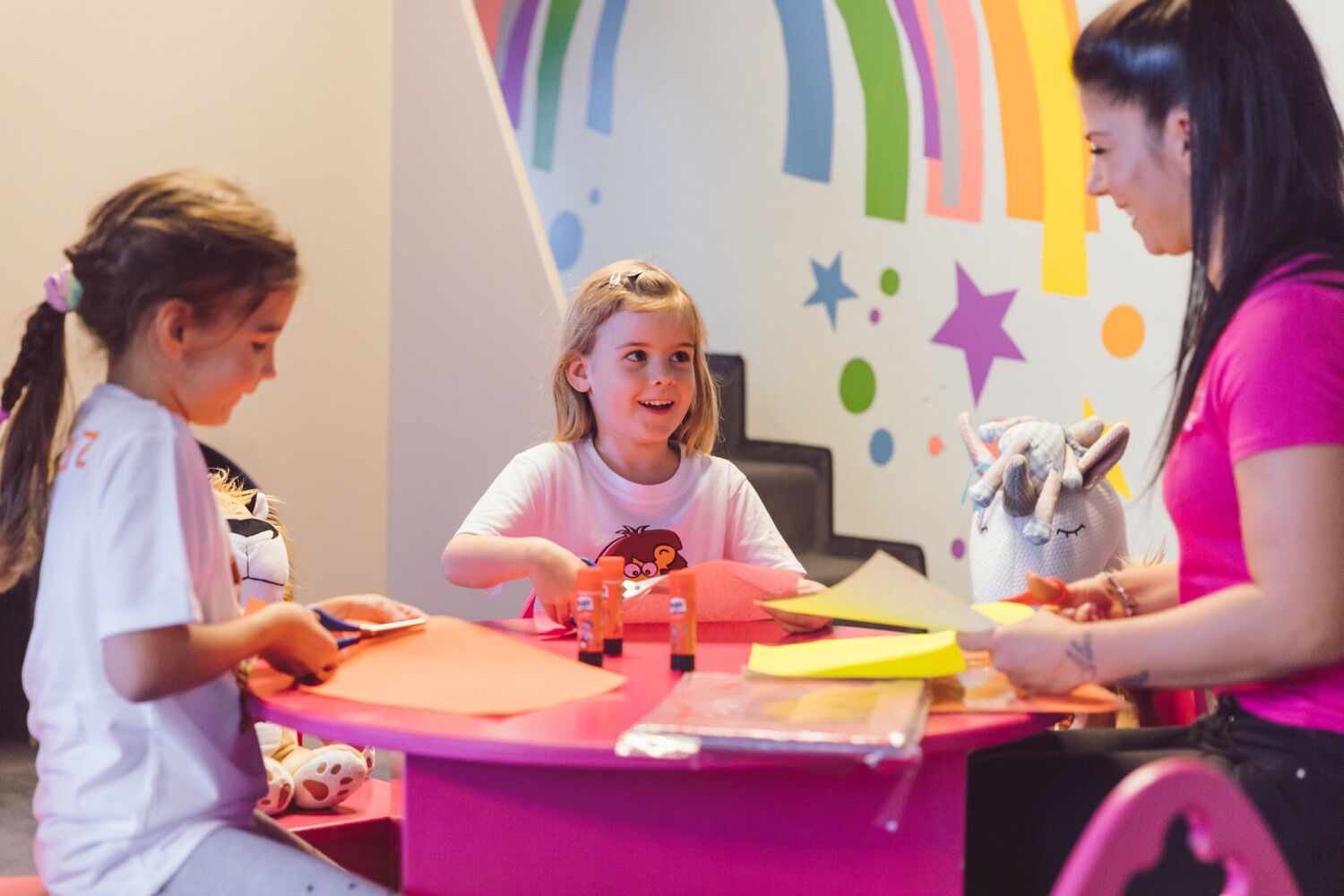 A group of children engaged in a craft activity at a table with colorful decorations and a plush toy.