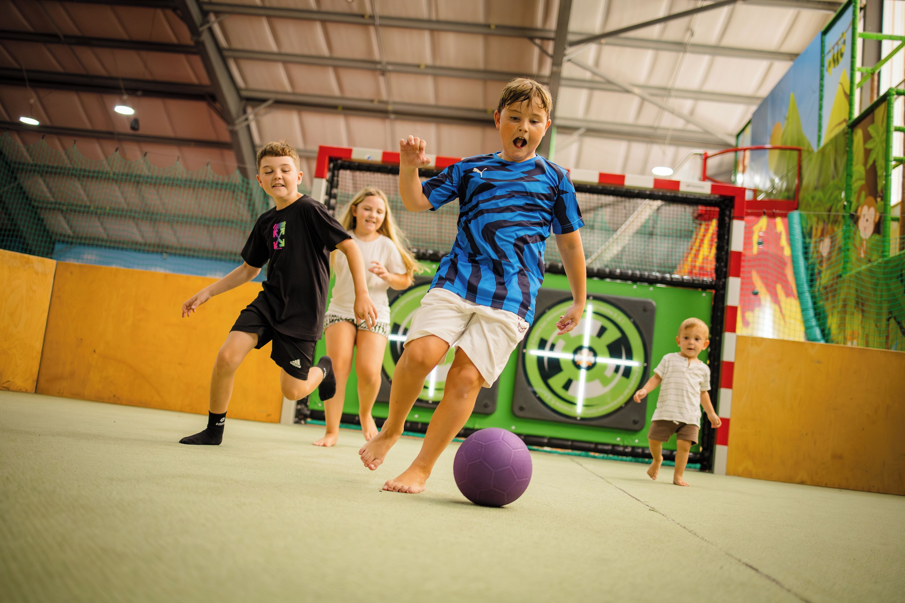 Un grupo de niños jugando fútbol dentro de un espacio cerrado.