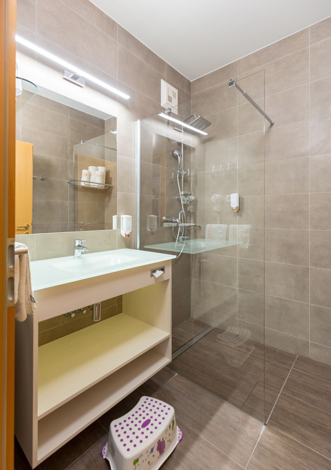 Un baño moderno con cabina de ducha de vidrio, un lavabo blanco y un mueble de tocador con espejo.