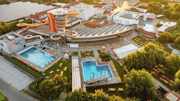 An aerial view of a resort with multiple swimming pools, water slides, and a large building with a unique cylindrical tower. - Thermenhotel Kurz (Lutzmannsburg)