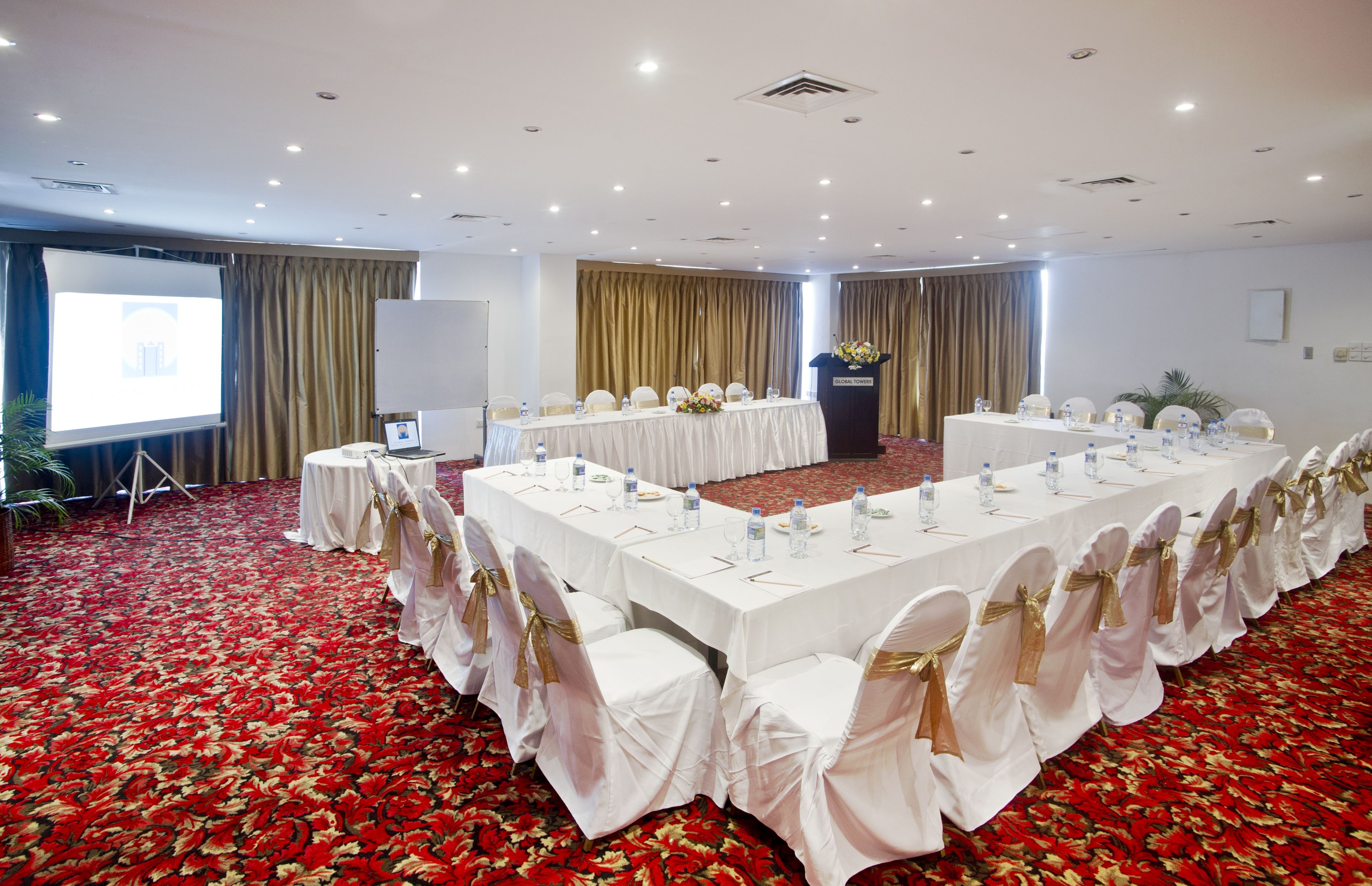 A conference room with a long table, white chairs with gold sashes, and a podium.