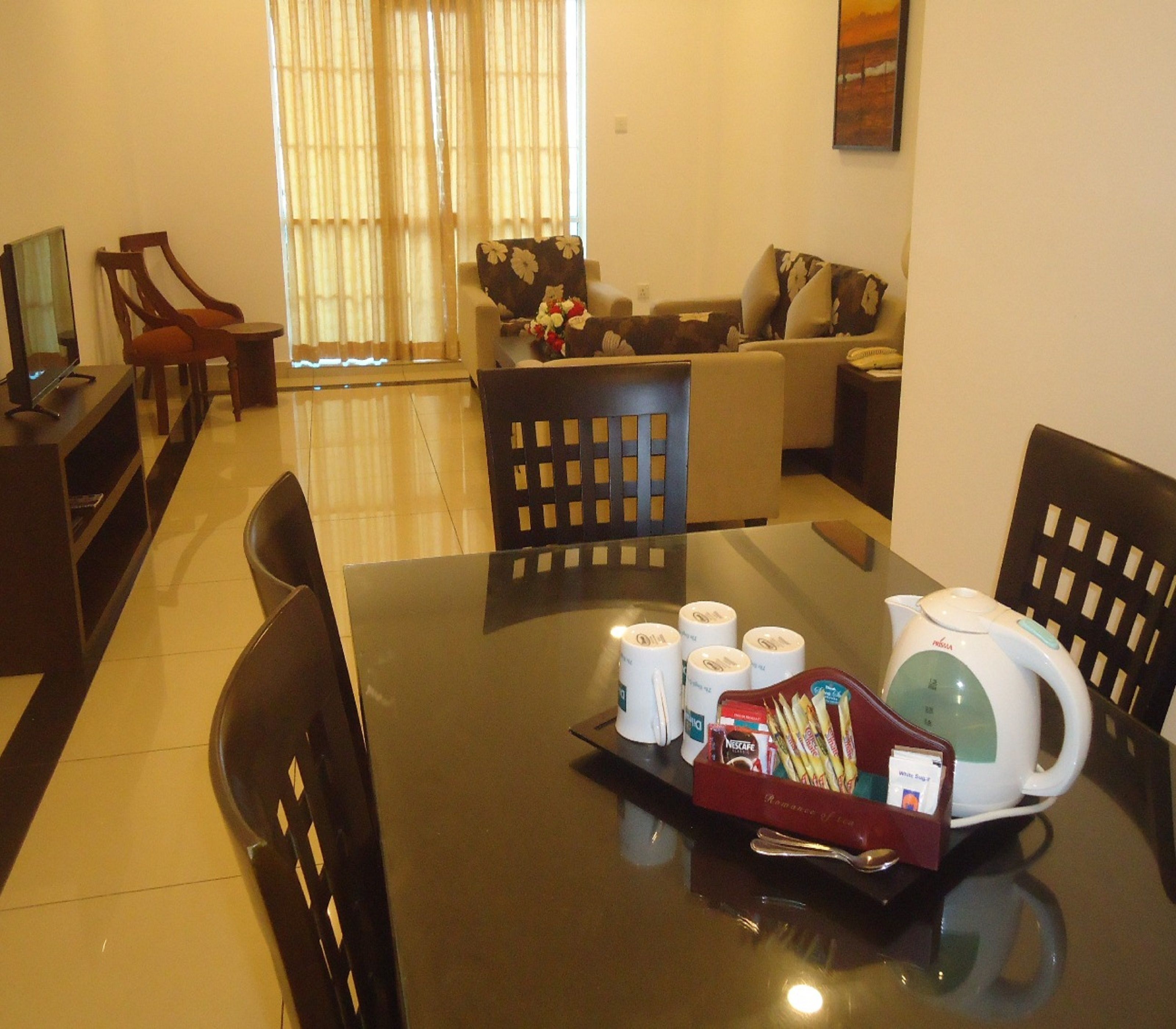 Un comedor con una mesa dispuesta para cuatro, que incluye una cafetera, tazas y una bandeja con aperitivos.