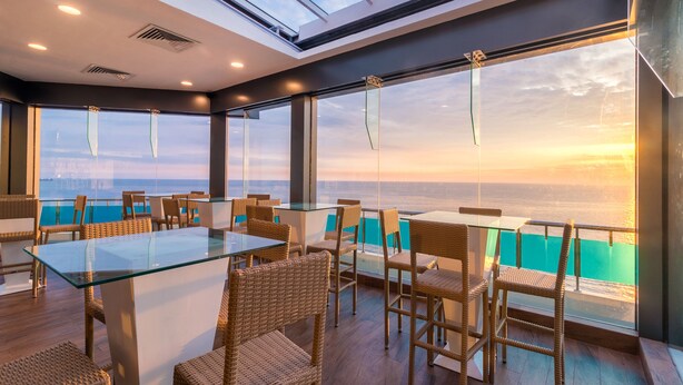 A modern dining area with glass tables and wicker chairs, overlooking a scenic ocean view. - Global Towers Hotel & Apartments (Colombo)
