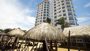 A hotel with multiple floors, a thatched-roof structure in the foreground, and a clear blue sky. - Global Towers Hotel & Apartments (Colombo)
