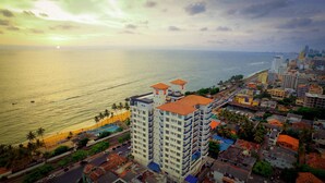 A coastal cityscape with a prominent hotel featuring multiple floors and balconies, situated near a beach and a busy road. - Global Towers Hotel & Apartments (Colombo)