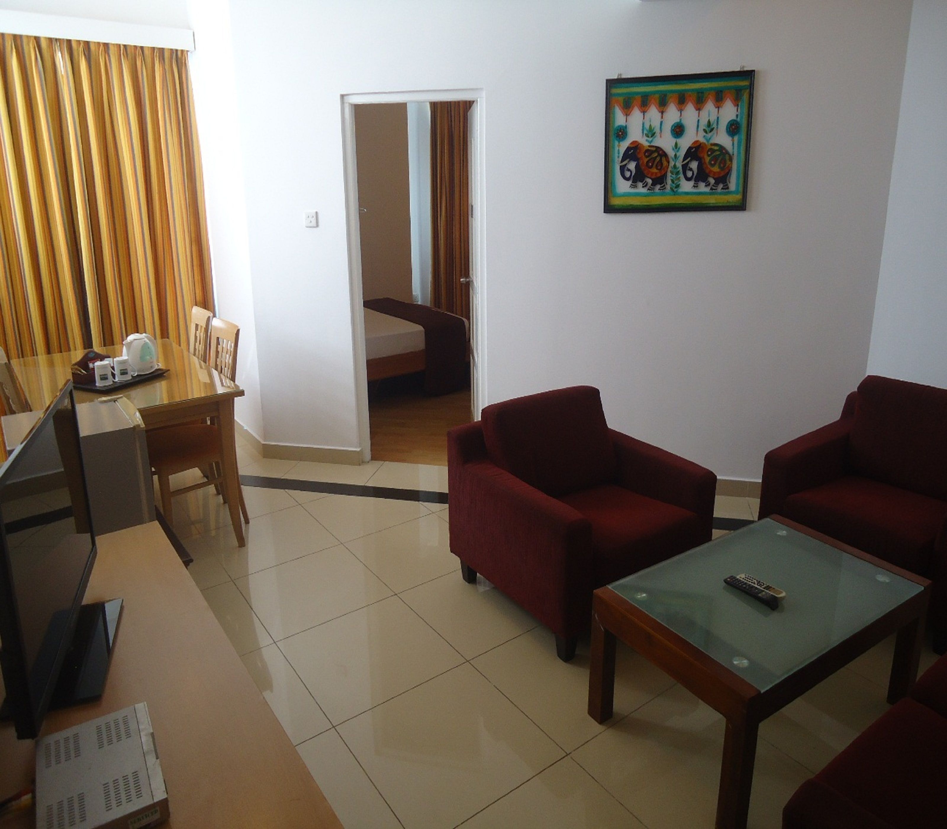 A hotel room with a dining area, two red sofas, a glass coffee table, and a painting on the wall.