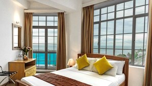 A hotel room with a large bed, a wooden desk, a chair, and a view of the ocean through large windows. - Global Towers Hotel & Apartments (Colombo)
