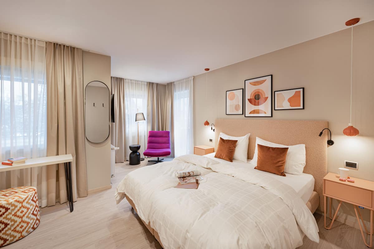 Ein modernes Hotelzimmer mit einem großen Bett, einem Schreibtisch, einem Stuhl und Kunstwerken an den Wänden.