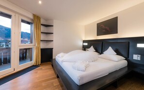 A modern hotel room with a large bed, a view of the mountains, and a balcony with curtains.