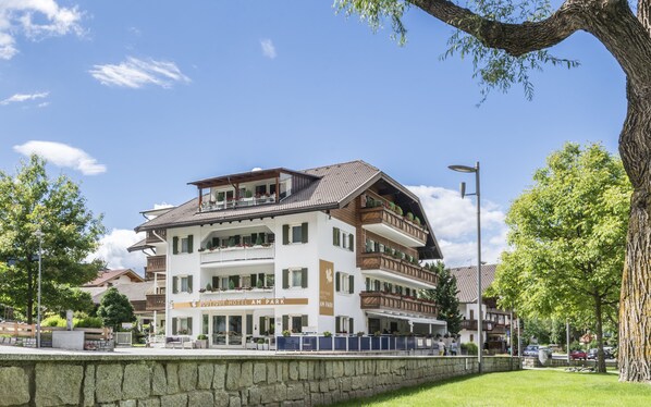 Un hôtel à plusieurs étages, doté de balcons, avec un mur de pierre à l’avant et un ciel d’un bleu limpide.