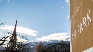 A sign for 'Boutique Hotel Am Park' with a clear view of a mountain and a church spire in the background.