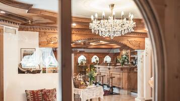 Vista attraverso una finestra su una stanza con soffitto in legno, un lampadario, un'area pranzo con tavolo apparecchiato per due e una cucina sullo sfondo.