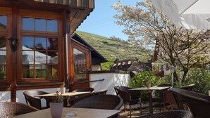 An outdoor seating area with wicker furniture and a table, overlooking a vineyard. - Hotel Altenberg (Baden-Baden)