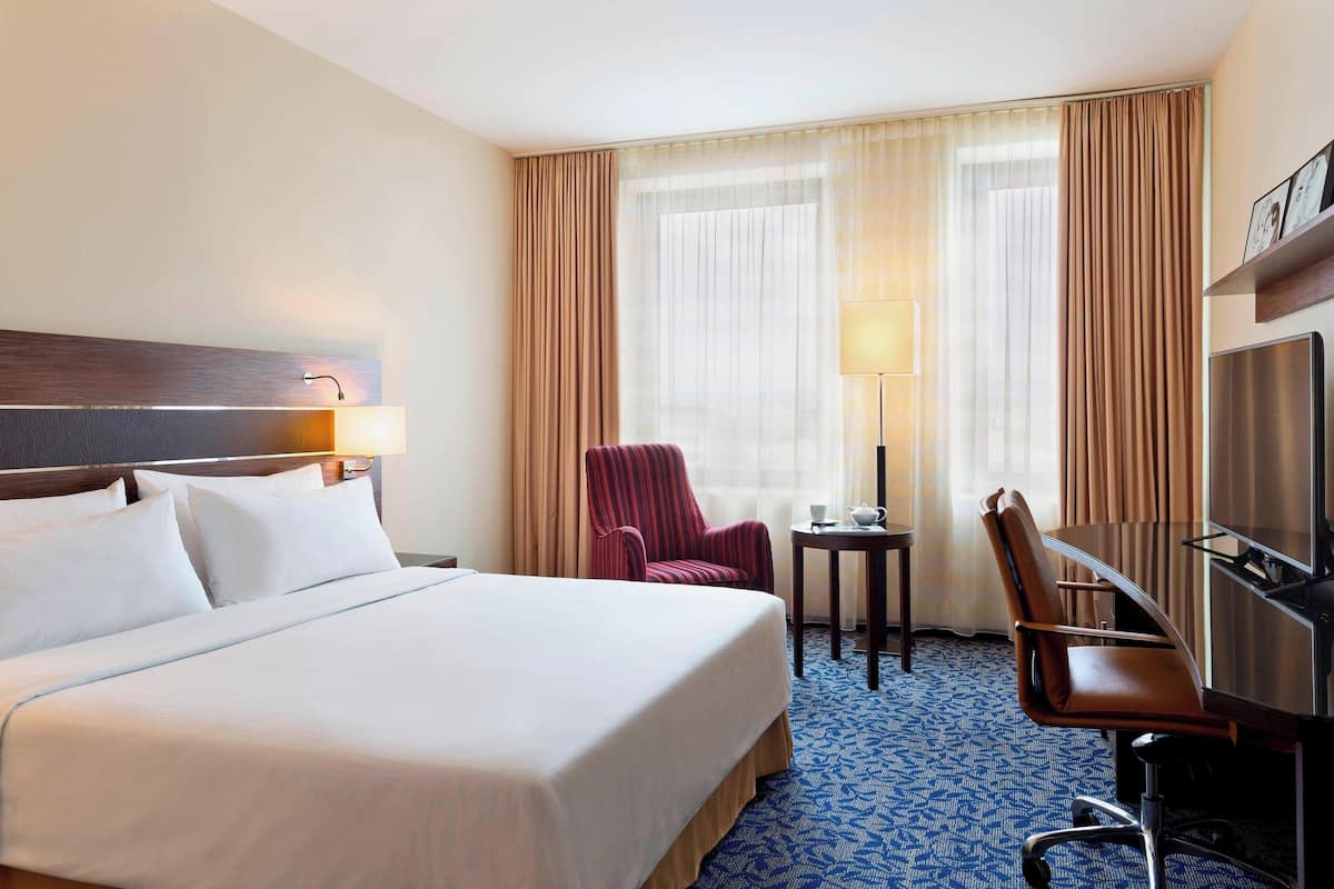 A hotel room with a large bed, a desk with a chair, a television, and a window with curtains.