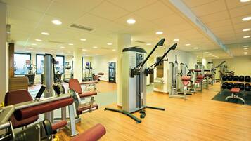 A gym with various exercise machines, a mirror, and a rack of dumbbells.
