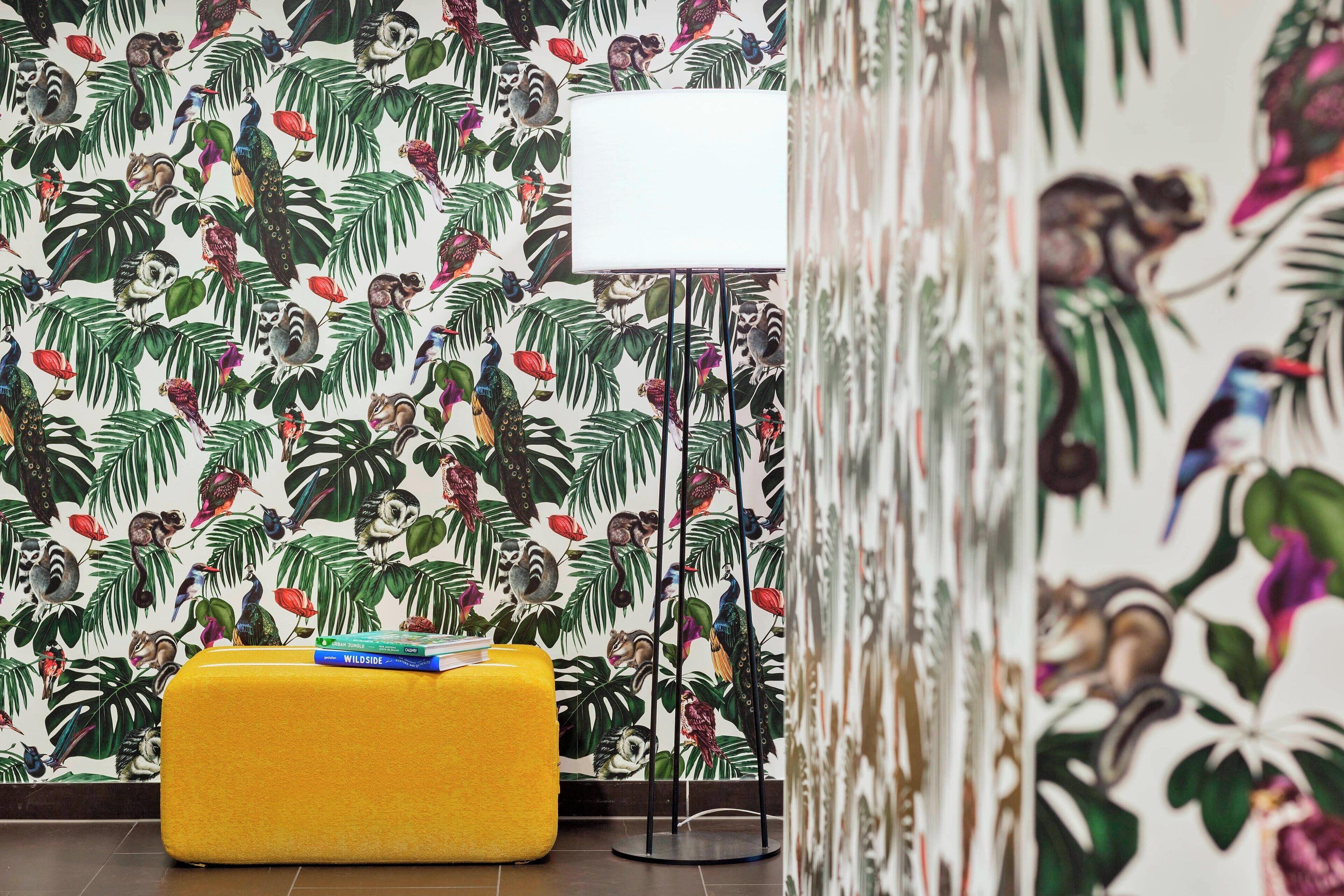 Ein Zimmer mit lebhaftem tropischen Wandpapier, einem gelben Hocker und einer Stehlampe.