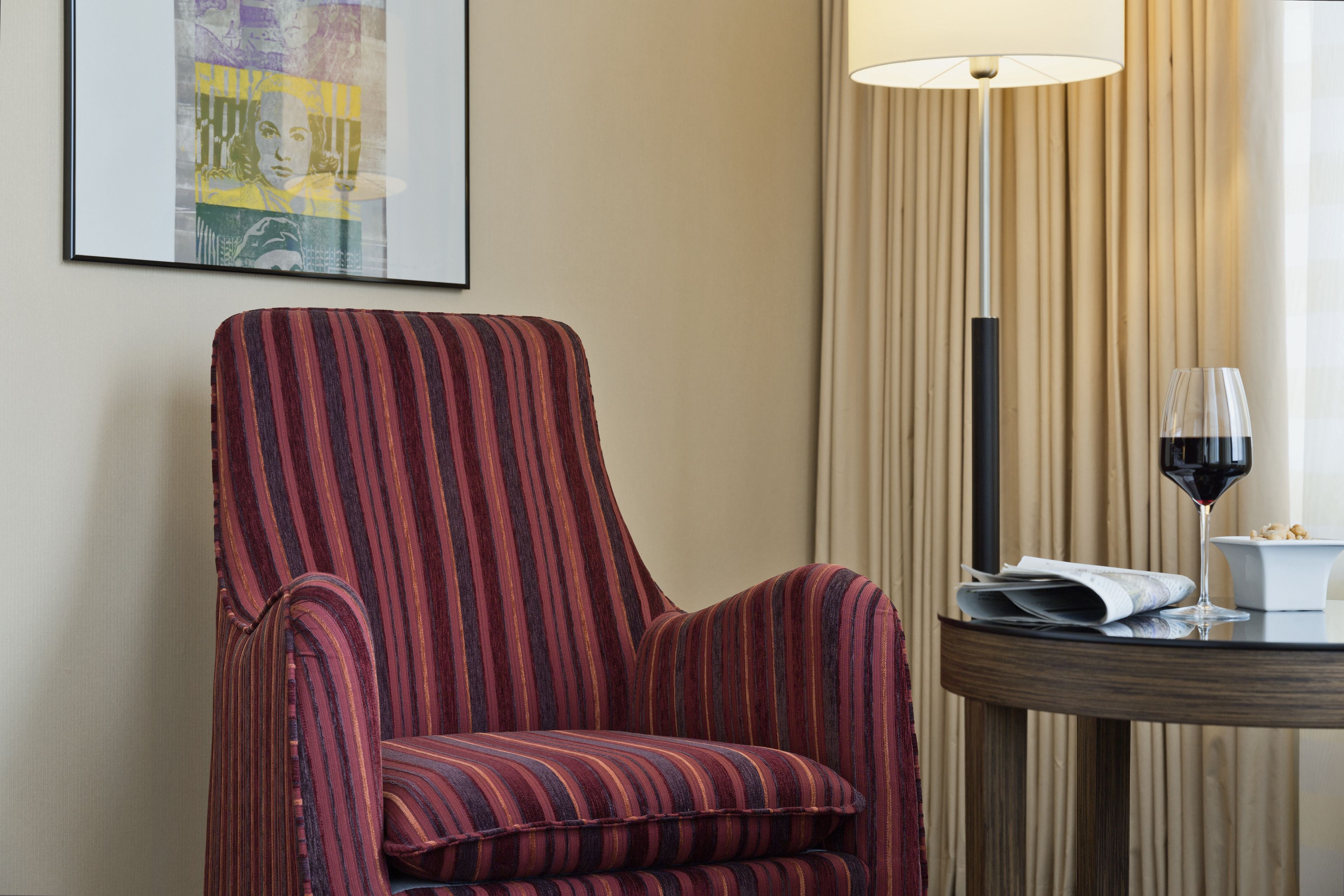 A striped armchair, a table with a wine glass and a bowl, and a lamp.