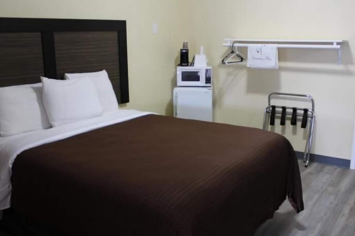 Quarto de hotel com cama, micro-ondas, pequeno frigorífico, porta-toalhas e cabideiro.