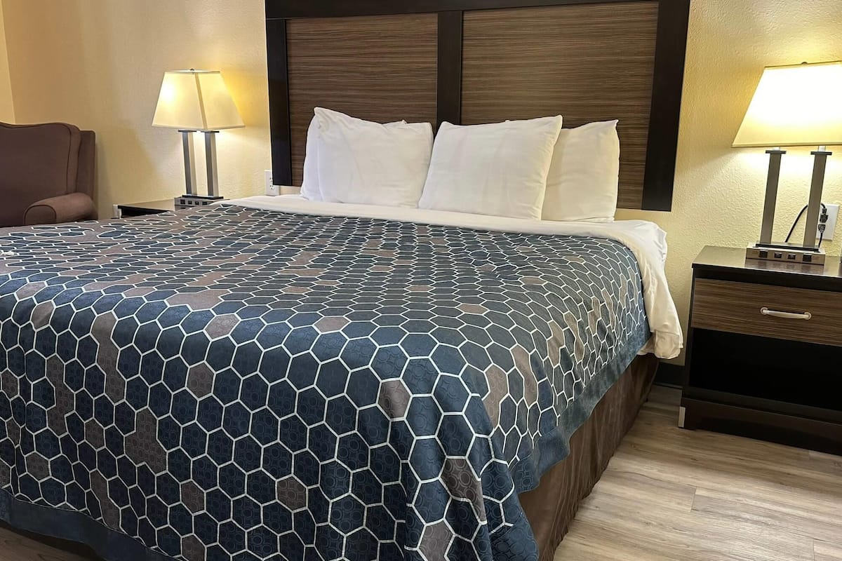 Quarto de hotel com uma cama grande, duas luminárias de cabeceira, mesa de cabeceira com relógio e uma cadeira.