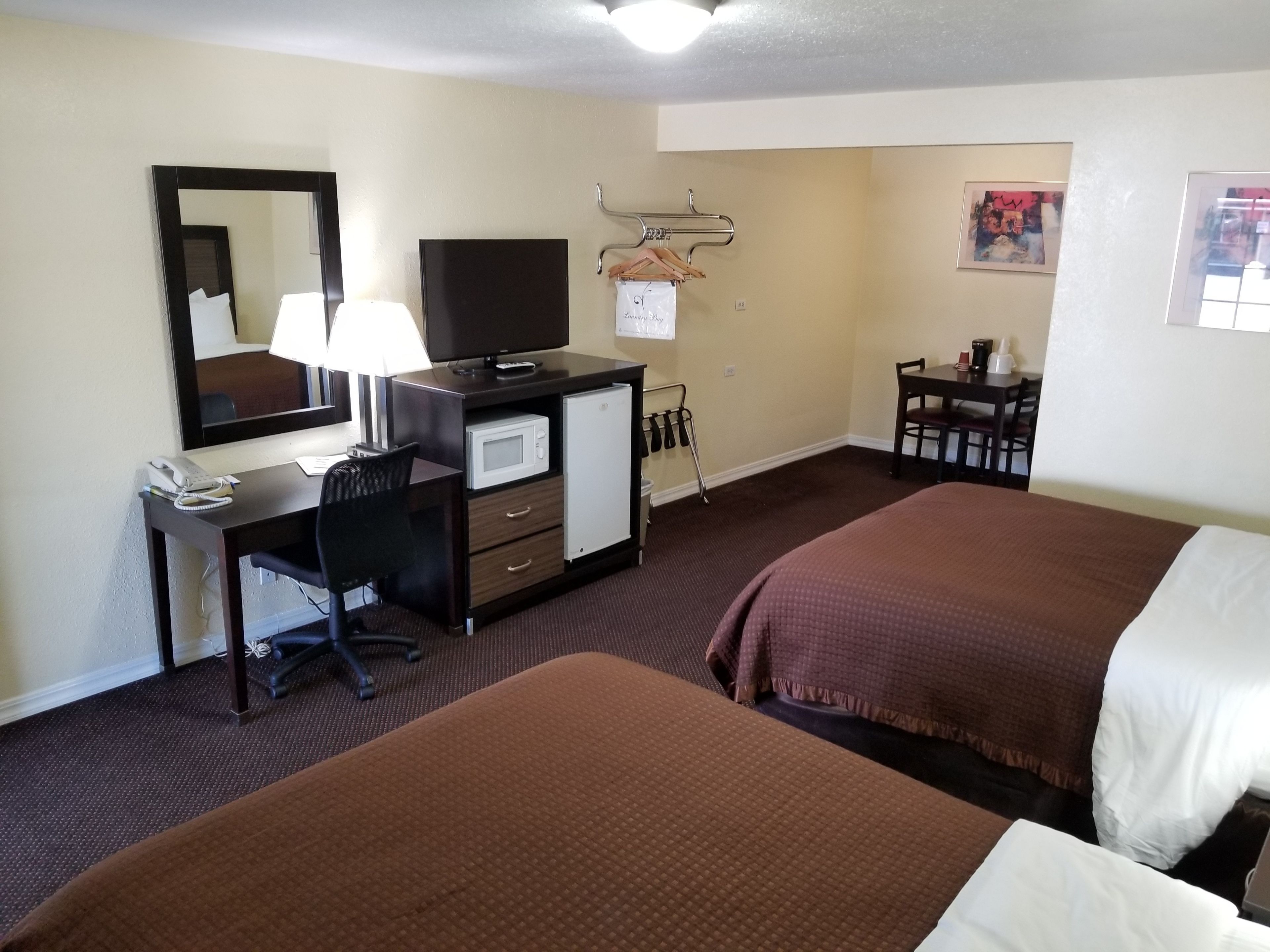 Een hotelkamer met twee bedden, een bureau met een computer, een magnetron, een telefoon en een televisie.