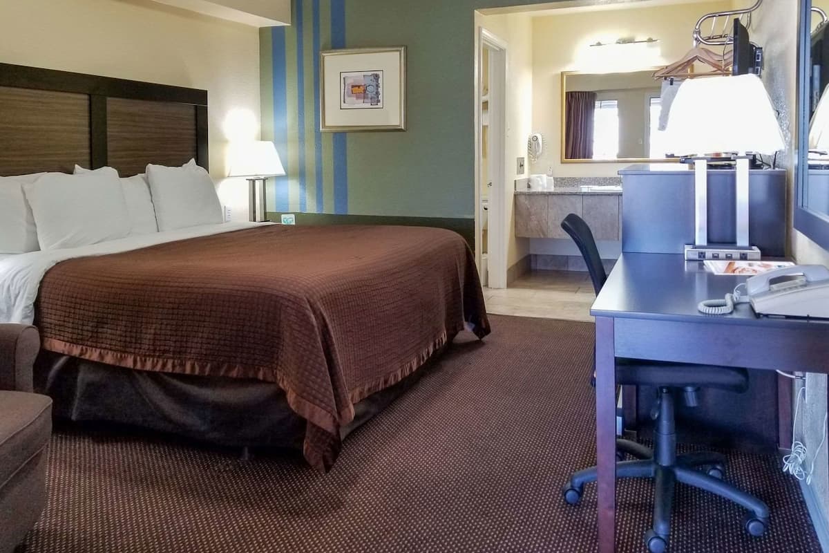 Quarto de hotel com cama, escrivaninha, cadeira e banheiro visível através de uma porta aberta.