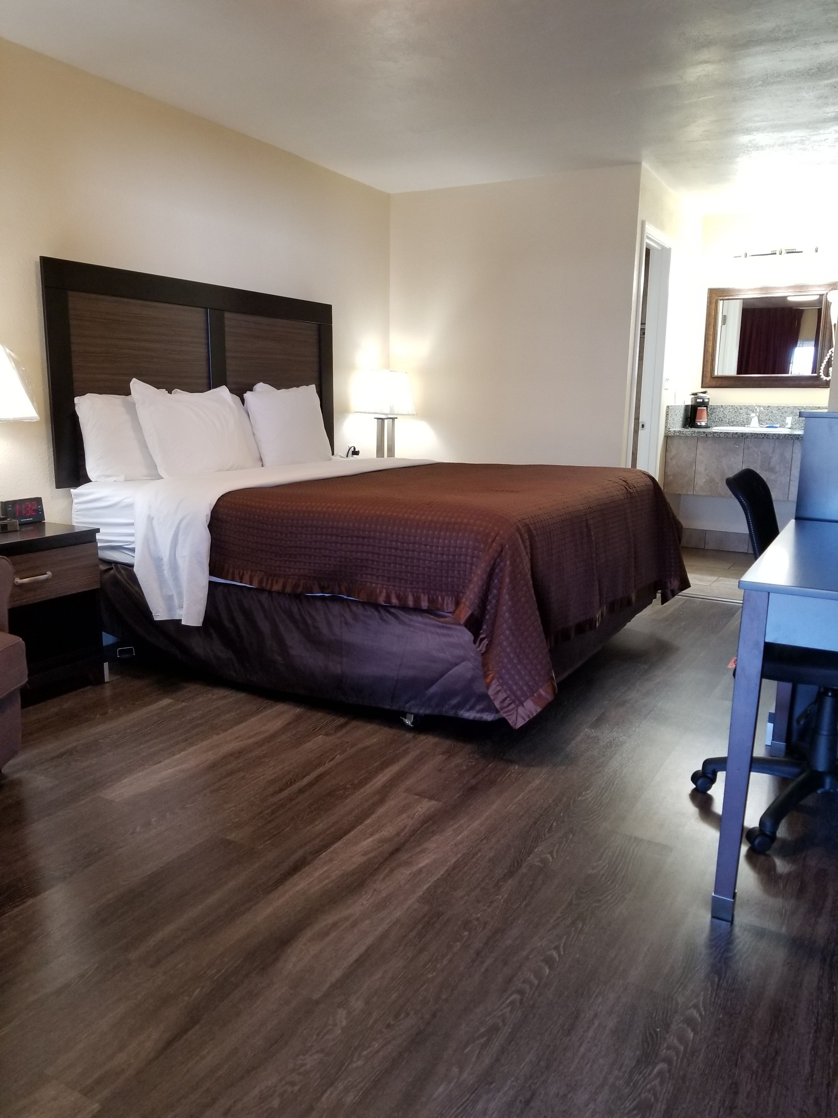 Hotelkamer met een groot bed, een bureau, een stoel, een nachtkastje, een lamp en een zichtbare badkamer door een geopende deur.