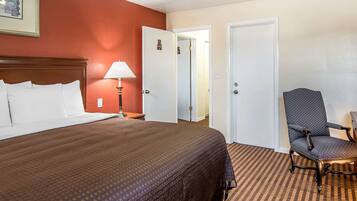A hotel room with a large bed, a chair, and two doors.
