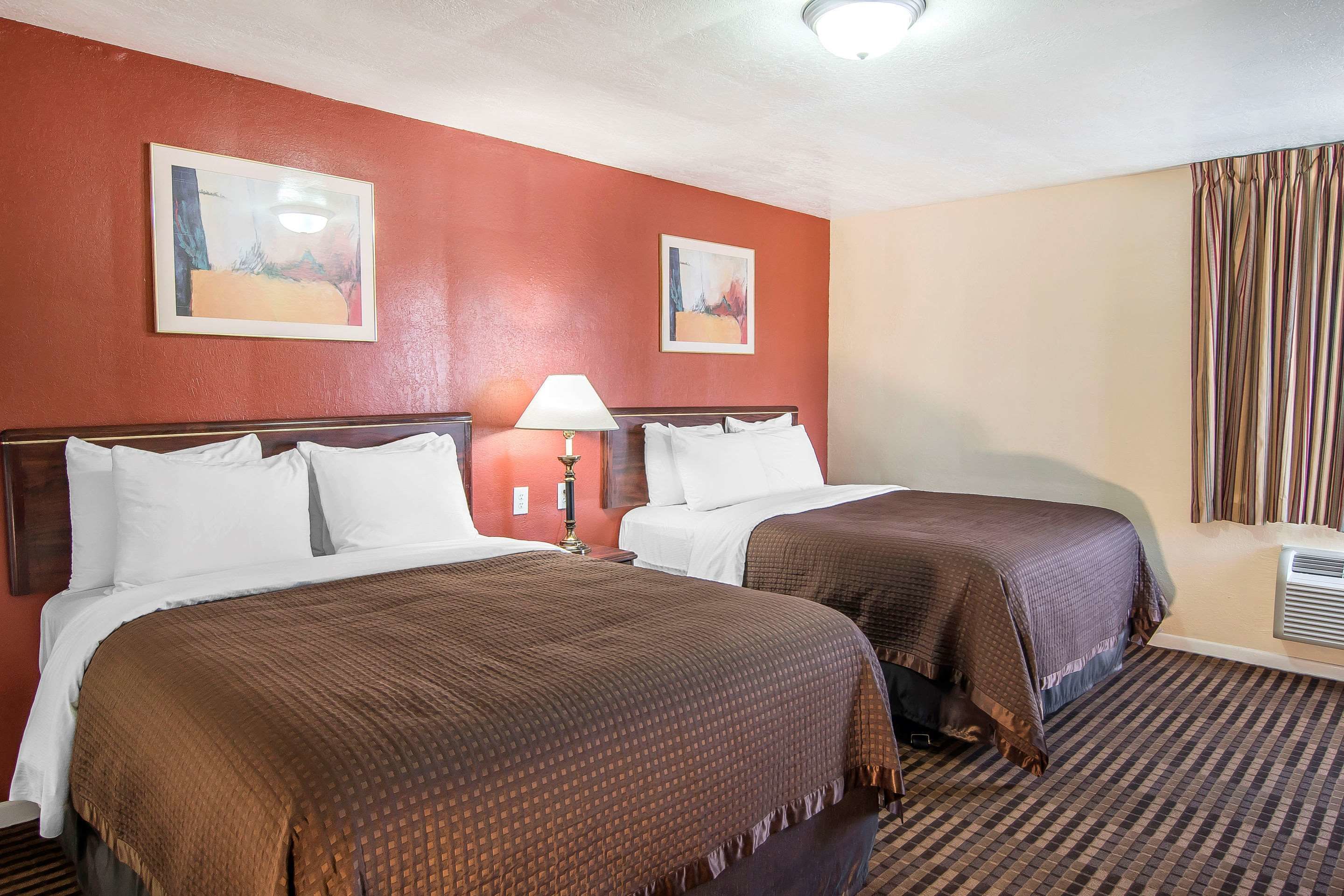 A hotel room with two beds, a lamp, and two paintings on the wall.