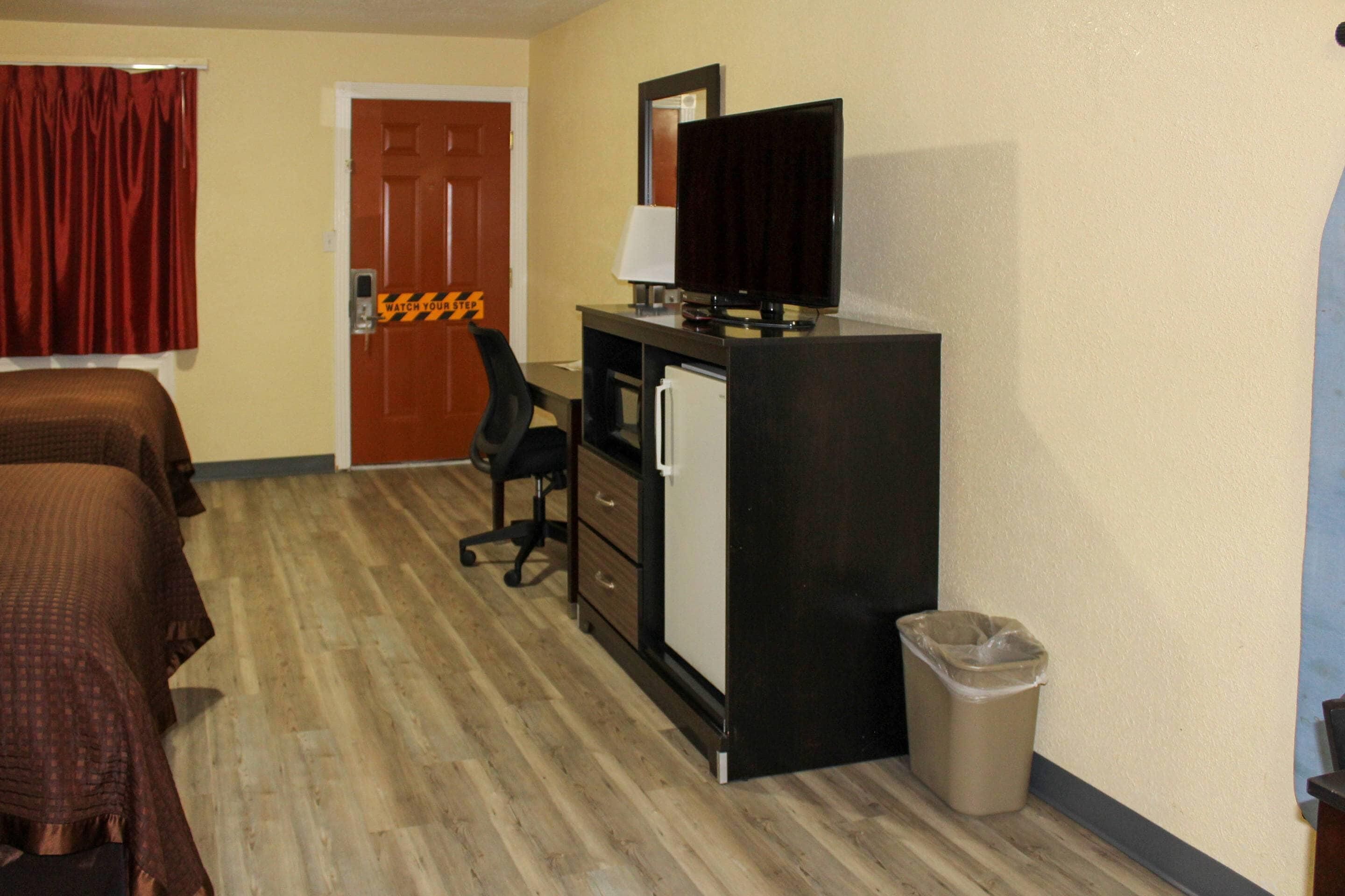 Habitación de hotel con una cama, un escritorio con computadora, una silla, un cesto de basura y una puerta.