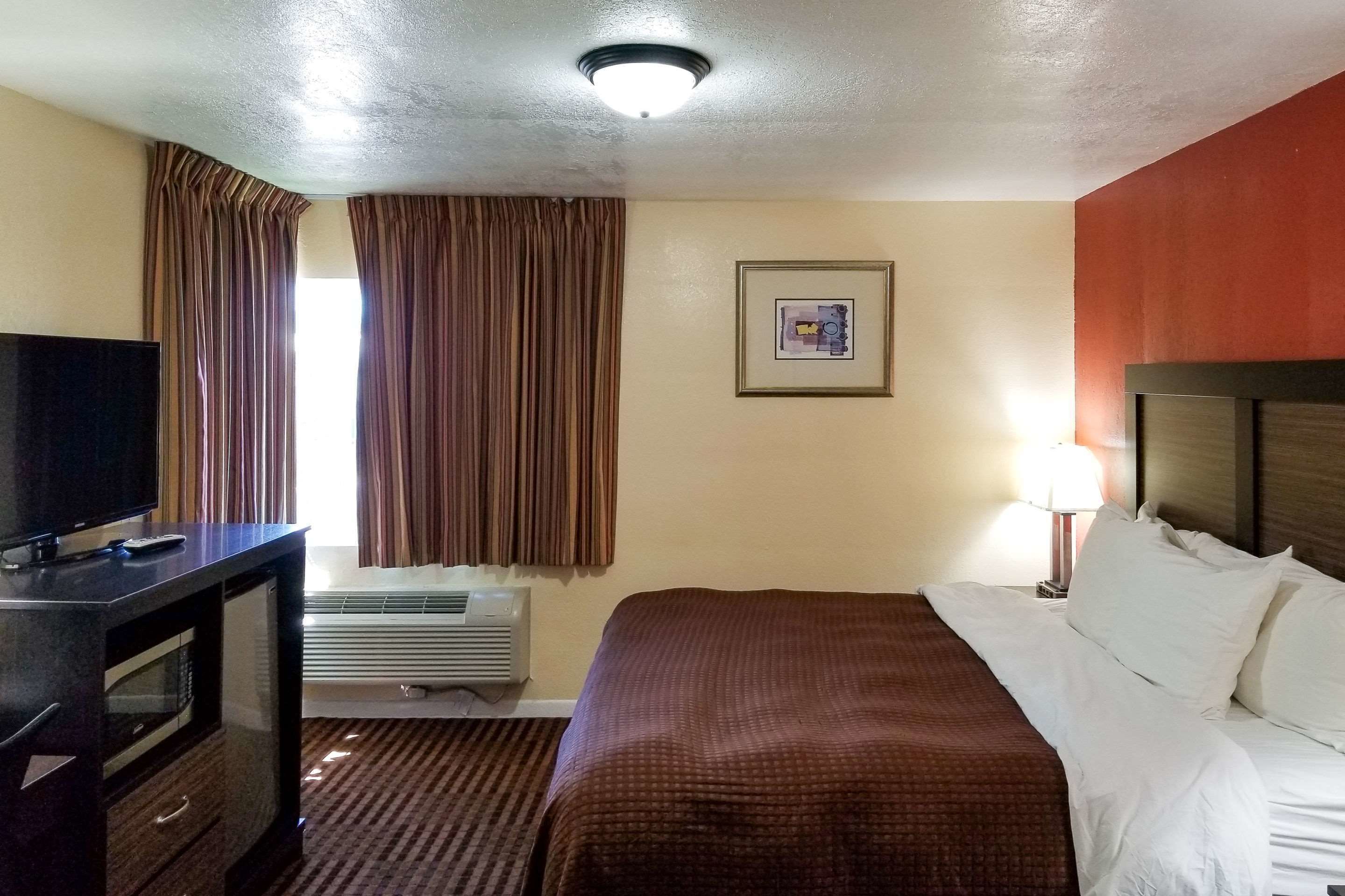 A hotel room with a bed, a TV, an air conditioner, a framed picture on the wall, and curtains.