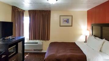 A hotel room with a bed, a TV, an air conditioner, a framed picture on the wall, and curtains.