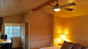 A wooden cabin room with a bed, a desk with a chair, and a window. - Alaska Glacier Lodge (Palmer)