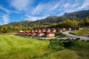 A row of wooden cabins with red roofs, set in a mountainous area with a clear sky.