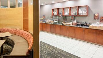 Eine Hotelhalle mit einer gebogenen Sitzecke, einem Buffet mit verschiedenen Speisen und einem gemusterten Teppich.